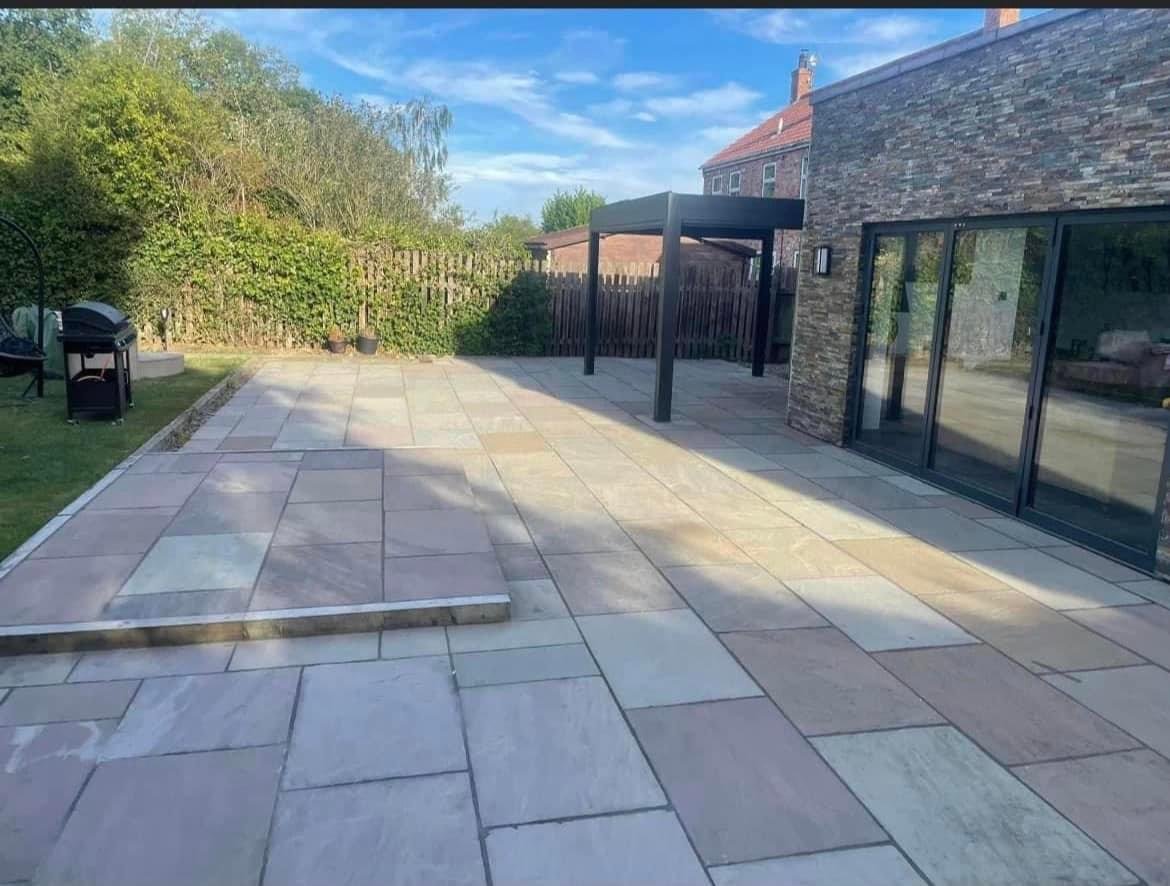 Broad mixed-tone patio beside a dark pergola and garden doors