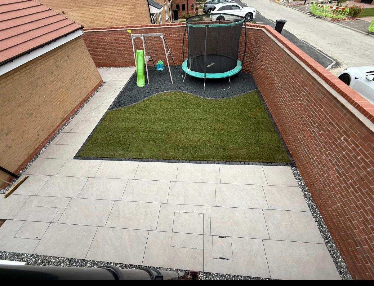 Lawn and pale patio within an enclosed brick-walled garden