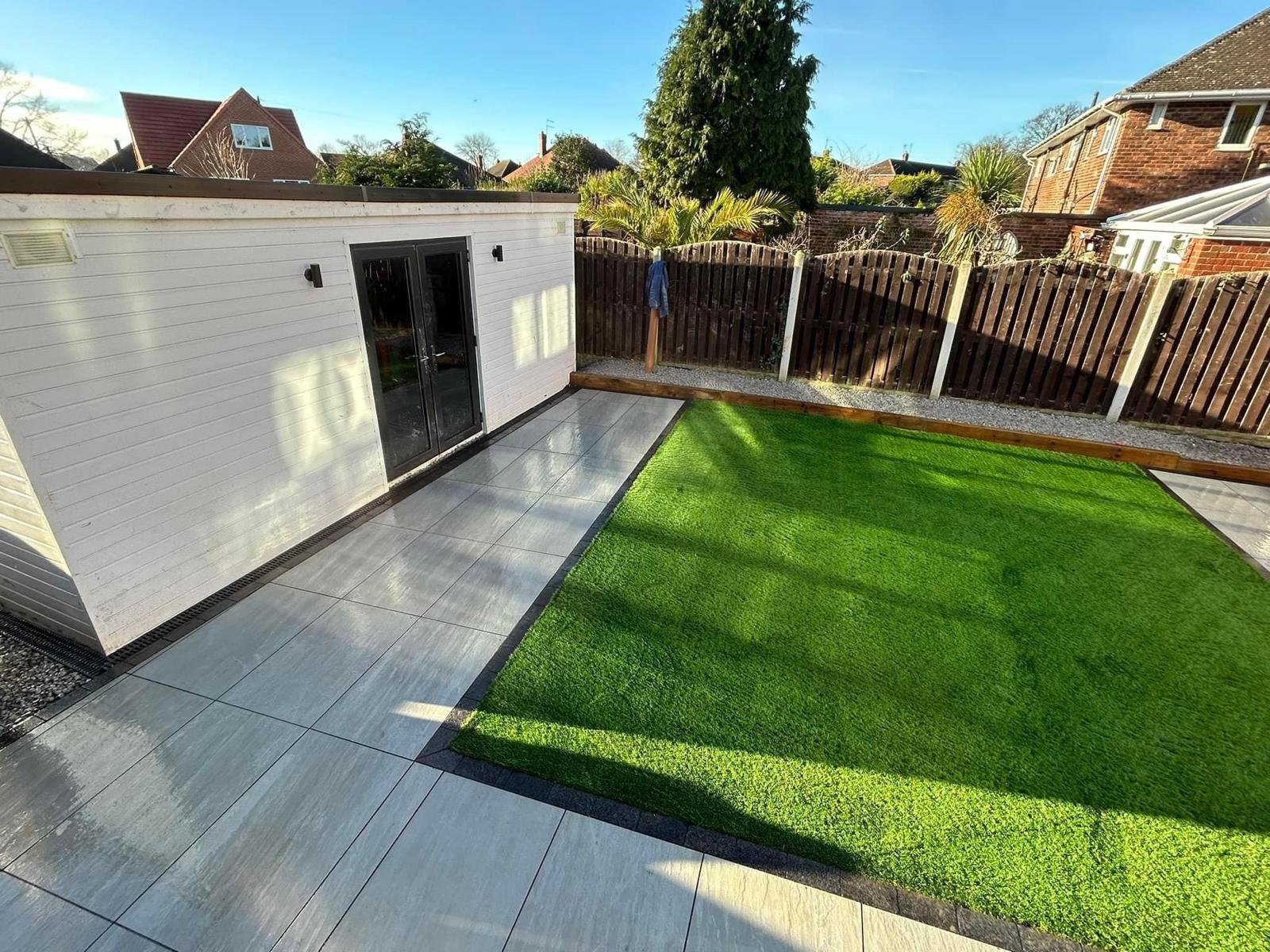 Green lawn and grey paving beside a white garden room