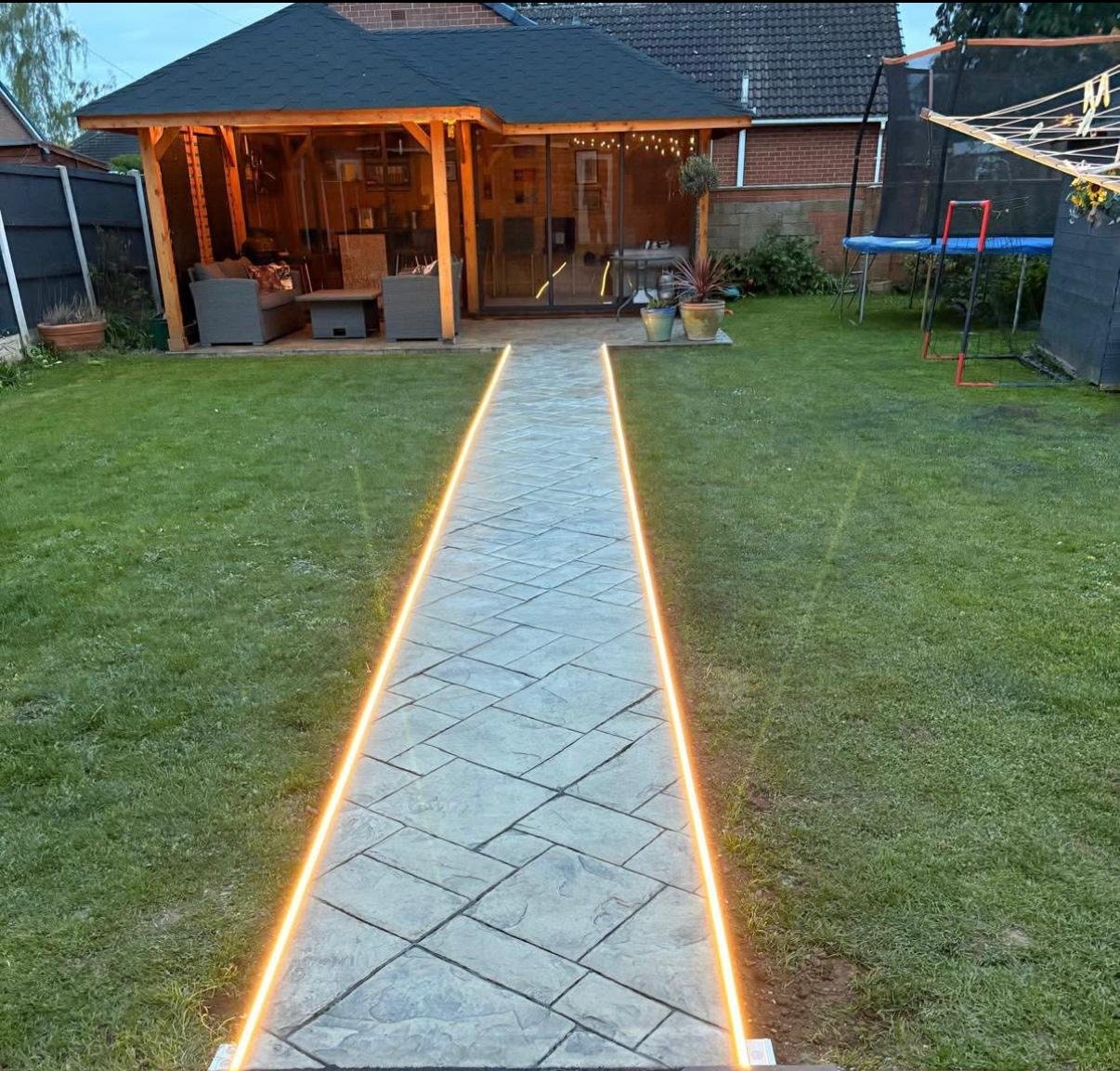 Illuminated patterned path across a lawn to a timber garden pavilion