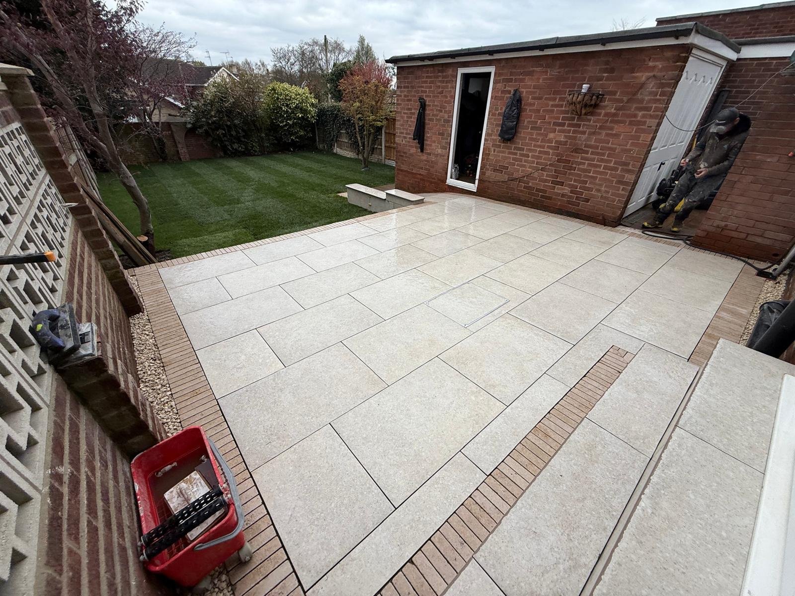 Pale patio paving beside a brick extension and lawn