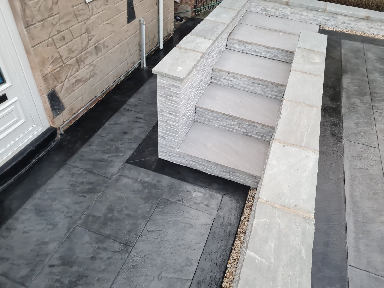 Pale steps with stone-faced side walls beside dark patterned paving