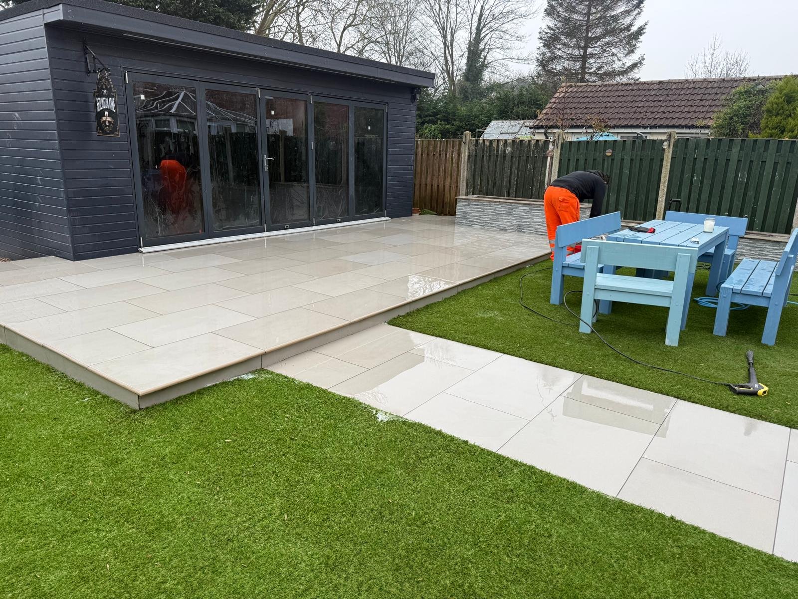 Work in progress beside a garden room, with pale patio paving and a lawn