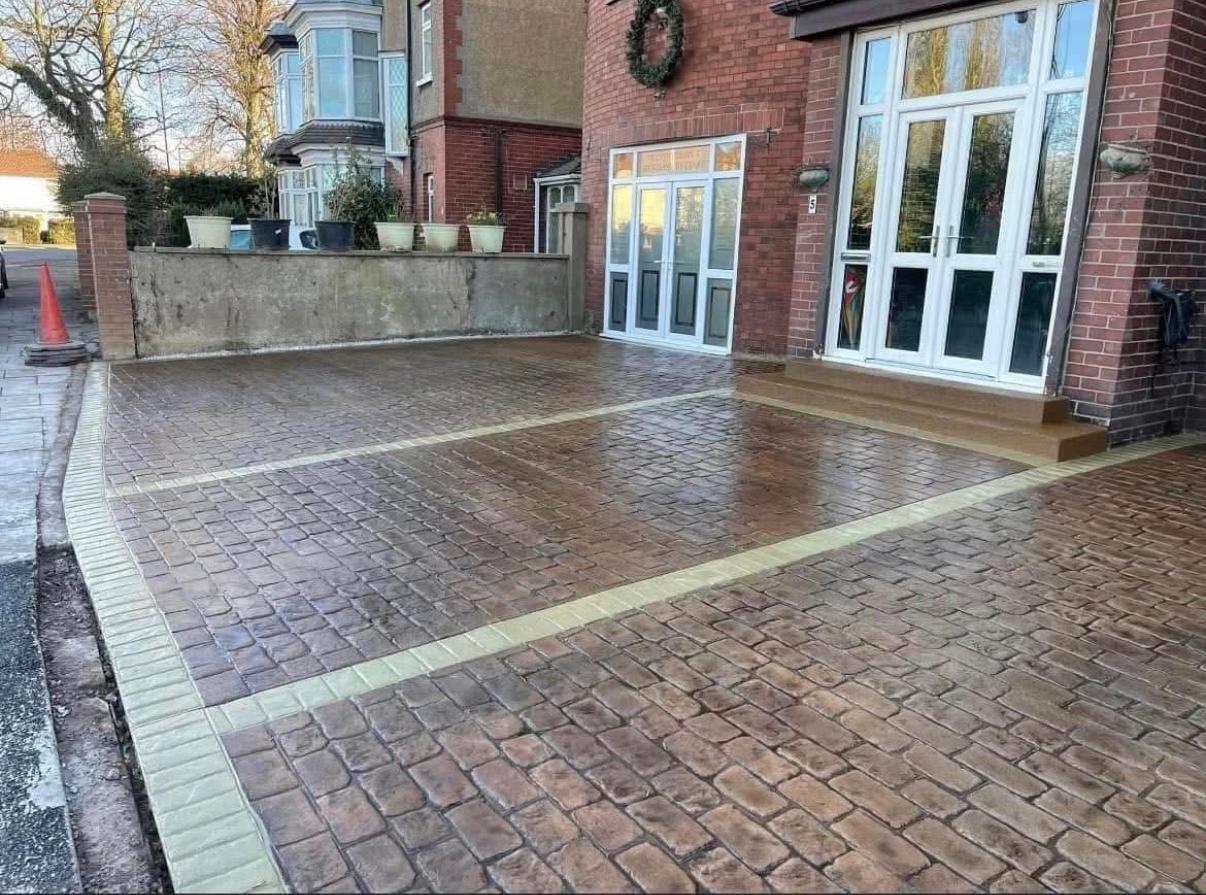Warm-toned patterned driveway with a contrasting pale border beside a house