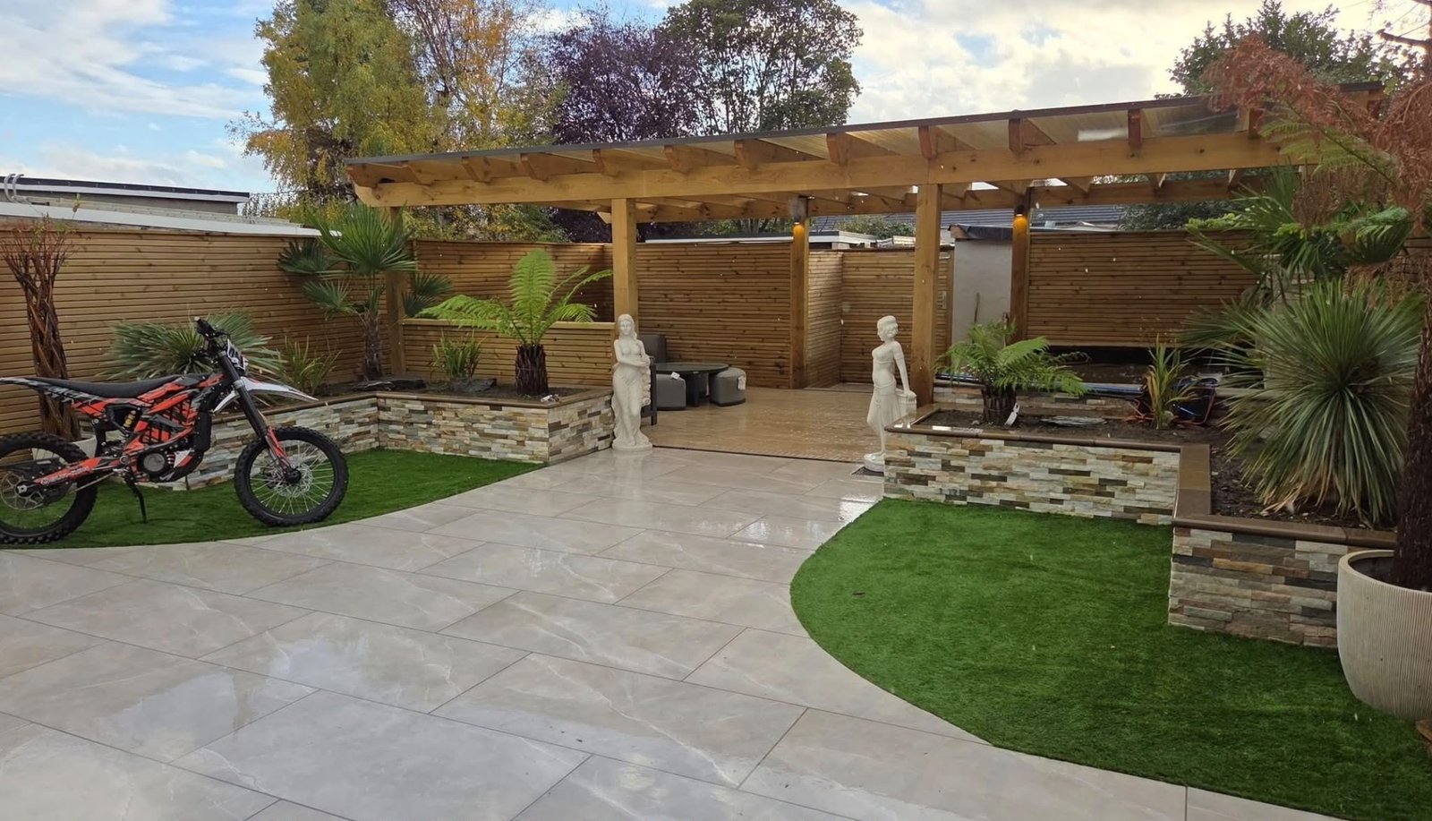 Completed garden with curved paving, lawns, stone-faced raised planters and a timber pergola