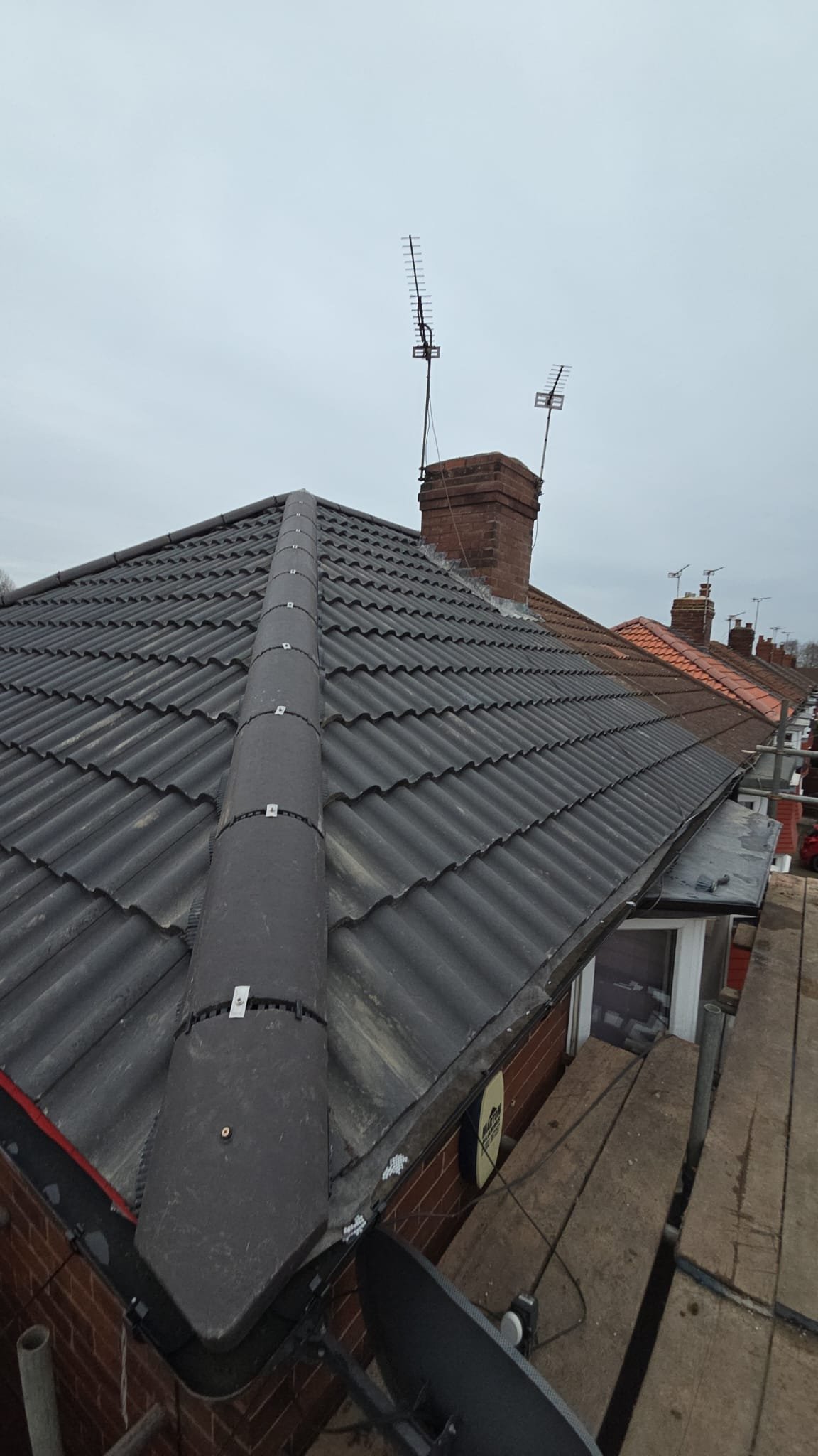 Grey tiled pitched roof and chimney viewed beside scaffolding